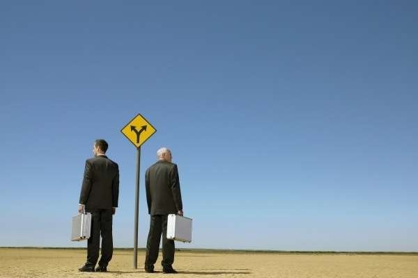 2 man in suits stand at a crossroads